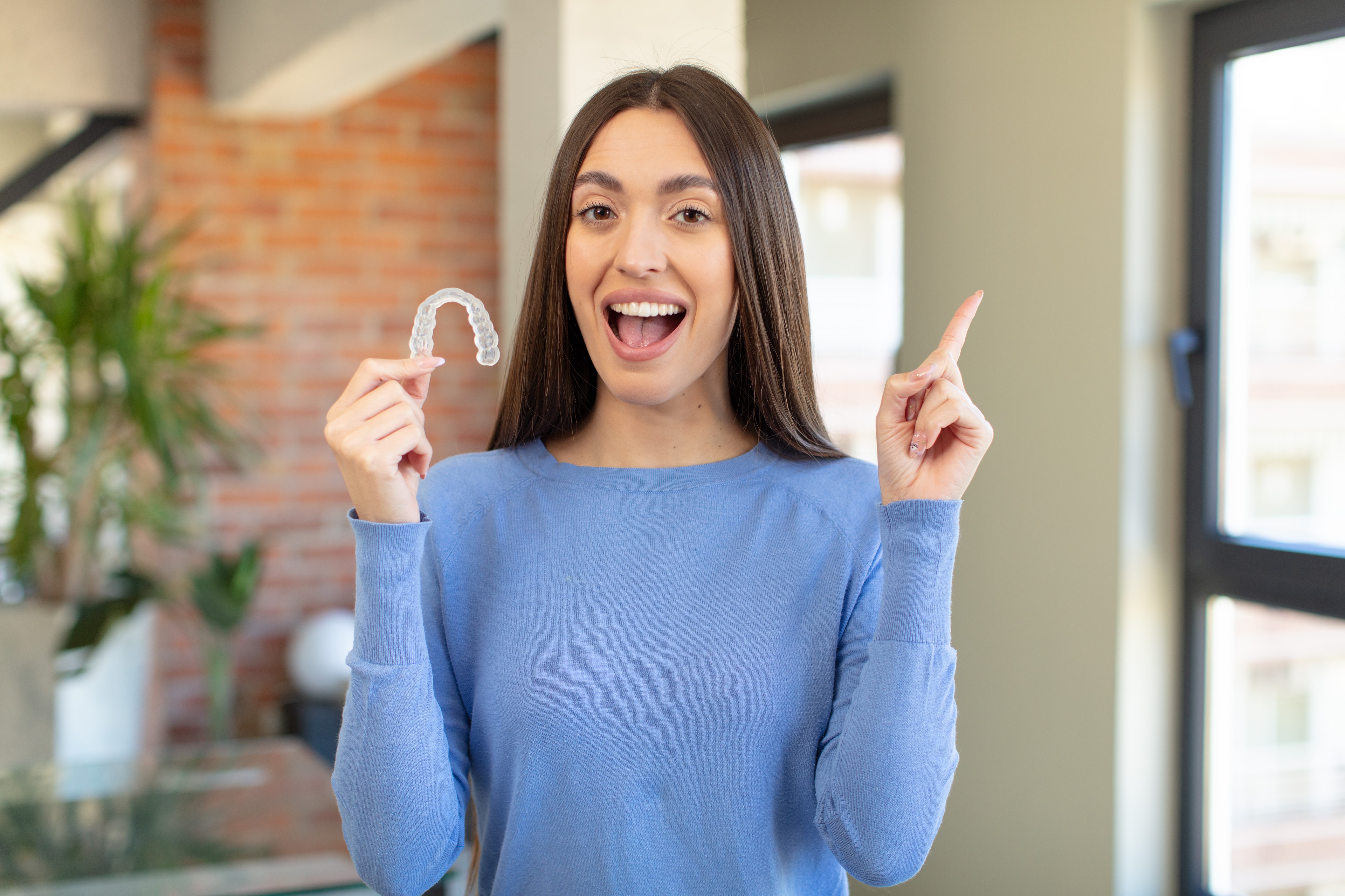 A patient smiling while holding a clear aligner