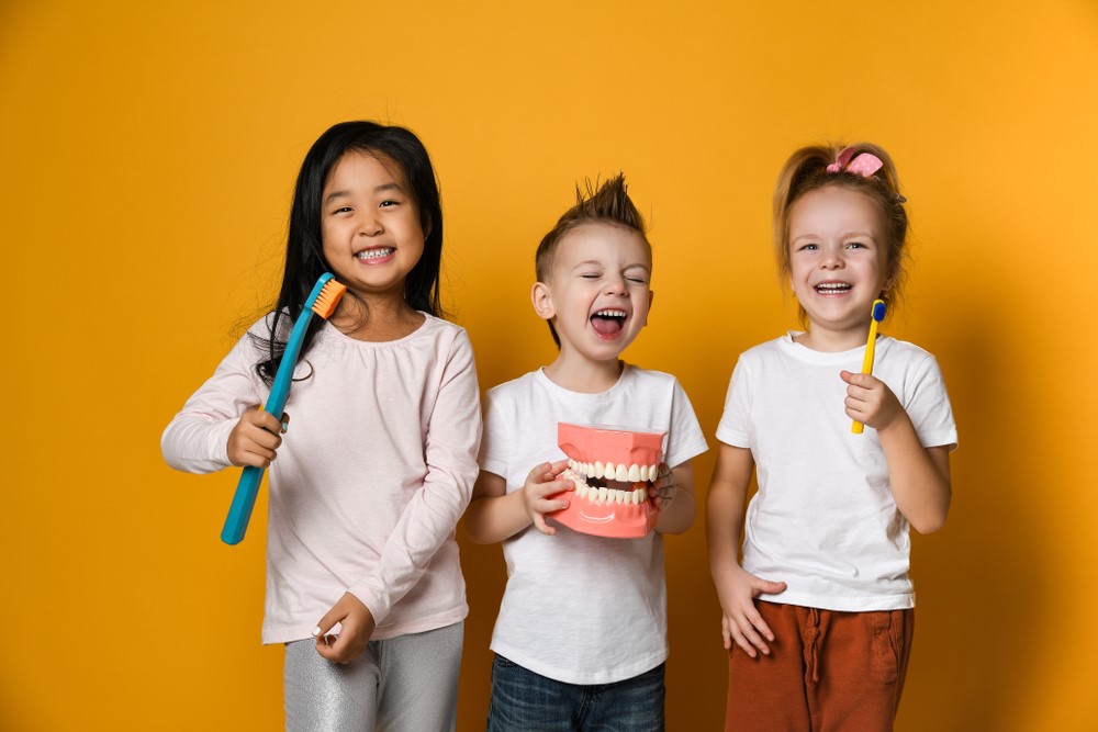 Two boys and a girl holding toothbrushes and smiling.